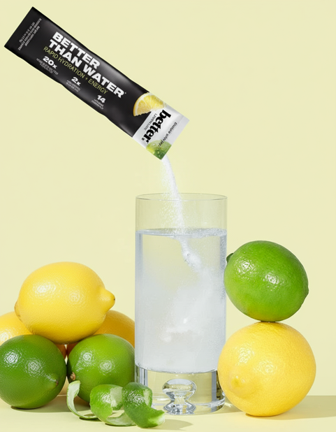 BETTER THAN Lemon Lime powder pouring into a glass, surrounded by fresh lemons and limes, on a Light green background